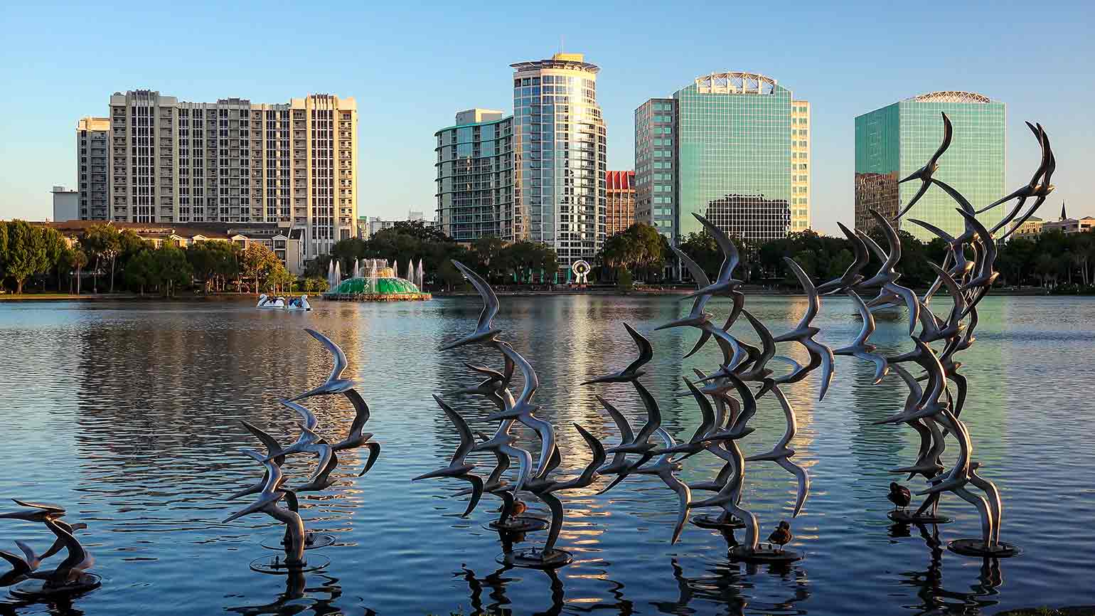 birds sculpture above water with city skyline