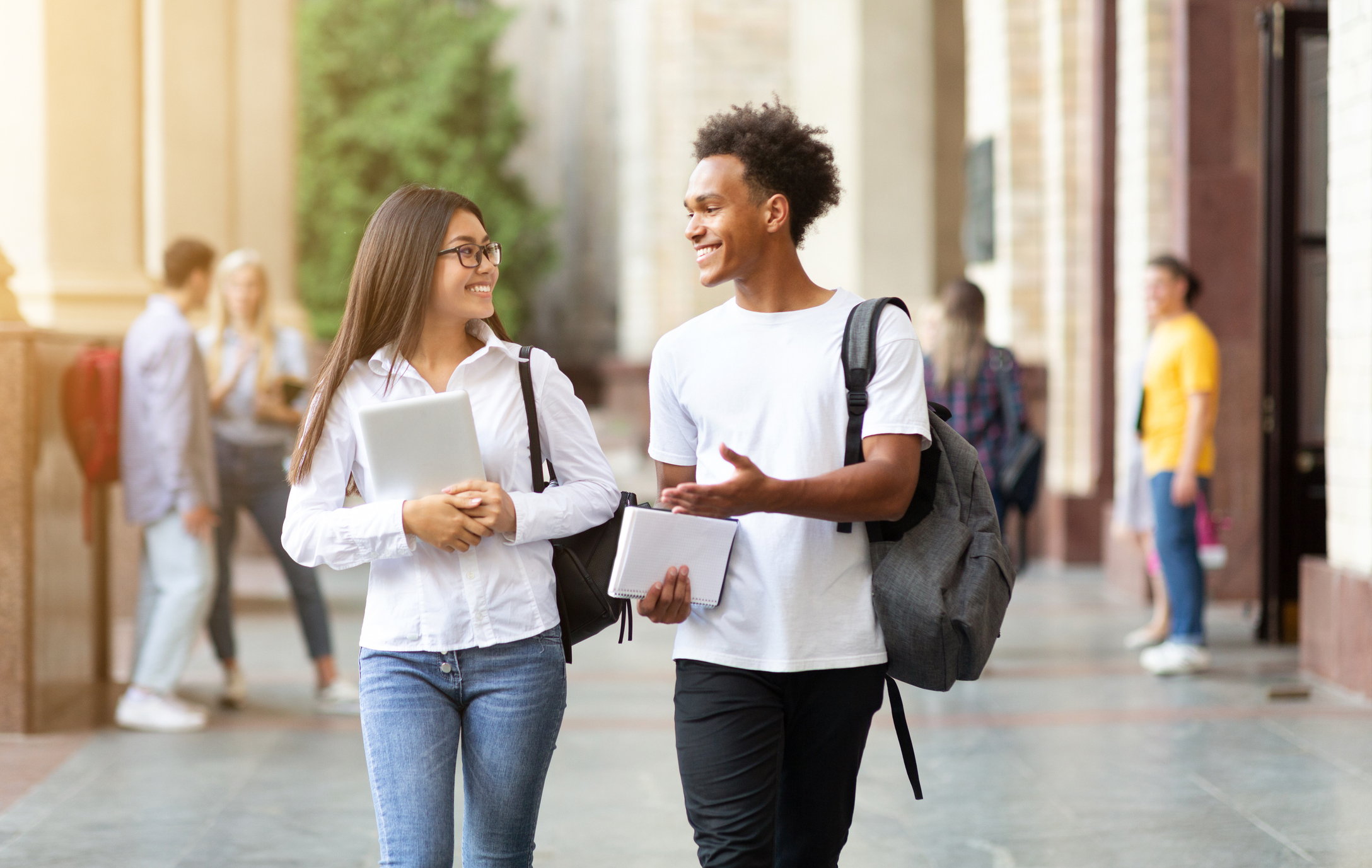 A female international student smiling, walking on campus with a Canadian classmate. 