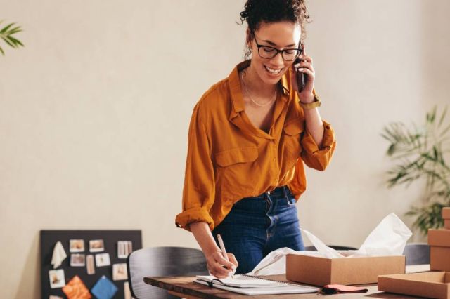 Female business owner on telephone packing boxes for shipping