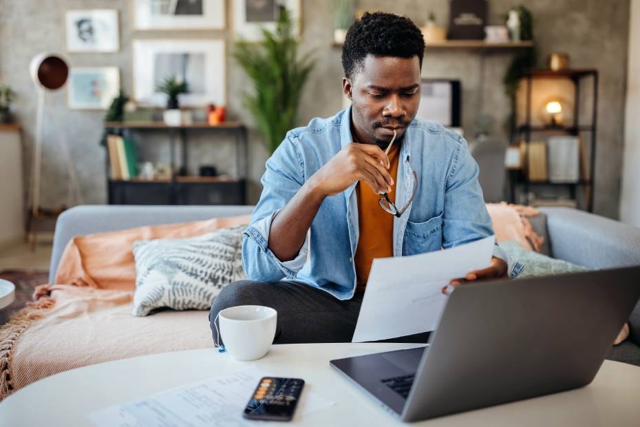 Man reading a piece of paper in front of an open laptop.