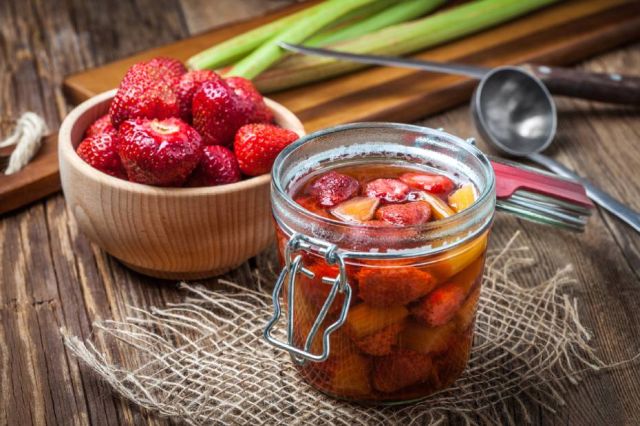 Homemade compote of rhubarb and strawberries on wooden table.