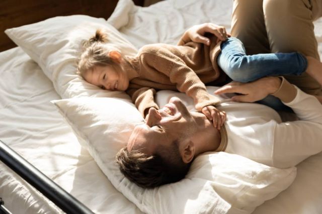 Happy father and little daughter relaxing in cozy bed together