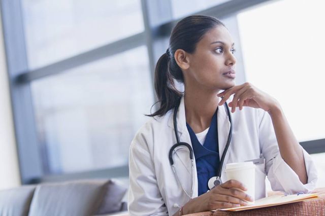 A picture showing a young female physician looking out the window thinking.