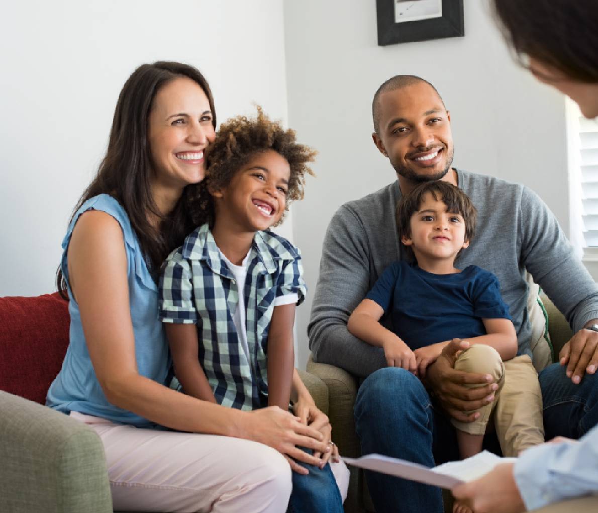 A young family of four with two sons sitting on a white couch, smiling while a mortgage specialist discusses moving mortgages for their home