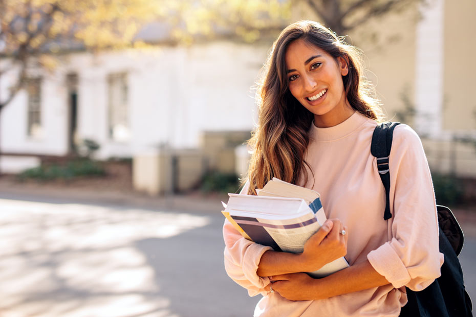 Beautiful young woman with backpack and books outdoors. College student carrying lots of books in college campus.