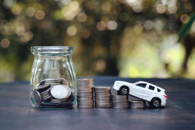 Series of stacked coins and toy car driving up the stacked coins on table