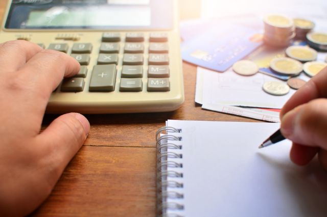 Hand on a calculator with credit cards and Canadian coins blurred in the background