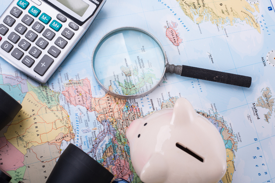 Map of the world with magnifying glass, piggy bank and calculator sitting on top