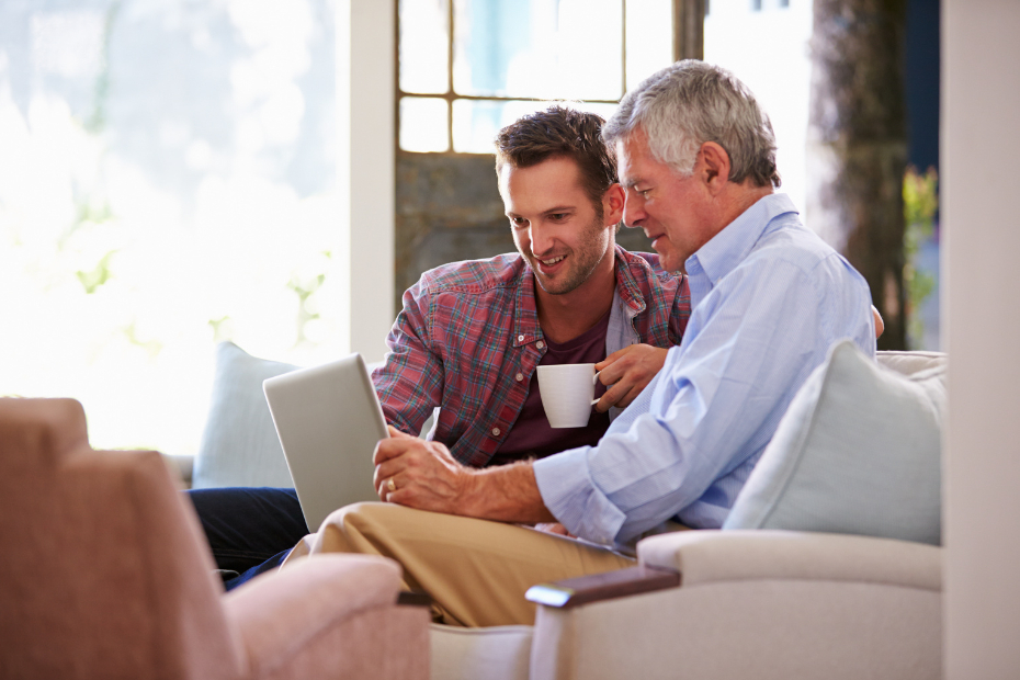 Father with his adult son on a sofa looking at budgets on a computer