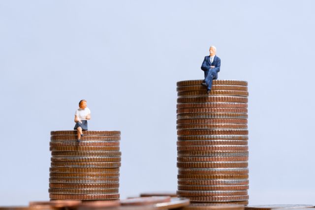 Miniature figurines of a woman on a small stack of coins and a well dressed elderly man on a larger stack of coins representing wealth gap