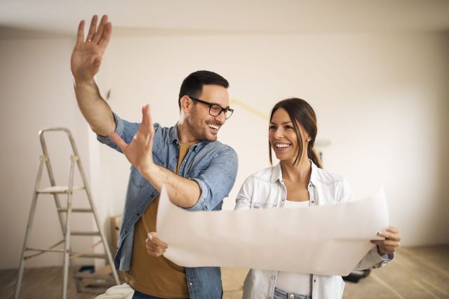 A happy couple looking at blueprint plans to renovate their home and add value