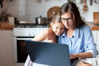 Une mère et sa fille souriantes s'embrassant, regardant un ordinateur portable