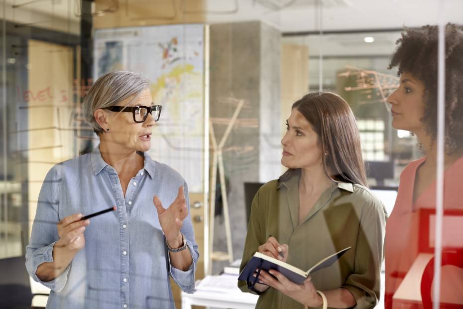 Trois femmes discutent à proximité d'un tableau blanc en verre.