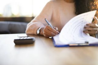 Une personne aux cheveux longs tourne la page d'un presse-papiers tout en prenant une note.