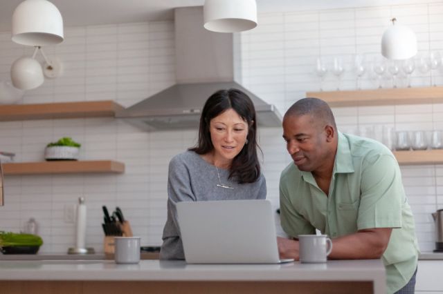 Image d'un couple heureux d'un certain âge qui regarde l'écran d'un portable placé sur le comptoir de cuisine.