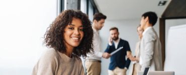 Une jeune femme souriante pointant vers l'écran de son ordinateur portable avec un collègue derrière elle