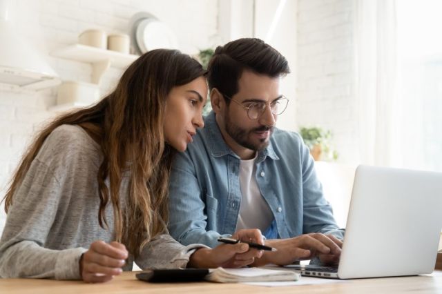 Jeune couple assis devant un ordinateur en train de regarder leurs finances