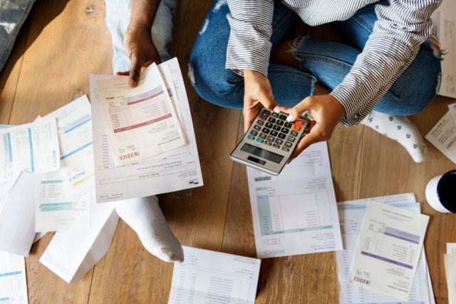 Gros plan de deux personnes assises par terre avec une calculatrice et des factures