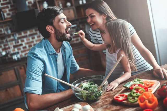 Un père, une mère et leur fille préparent ensemble un repas dans la cuisine.