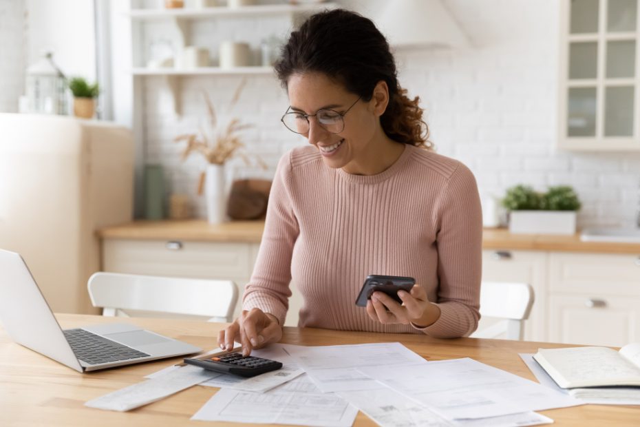 Jeune femme souriante à la maison avec des documents financiers et une calculatrice