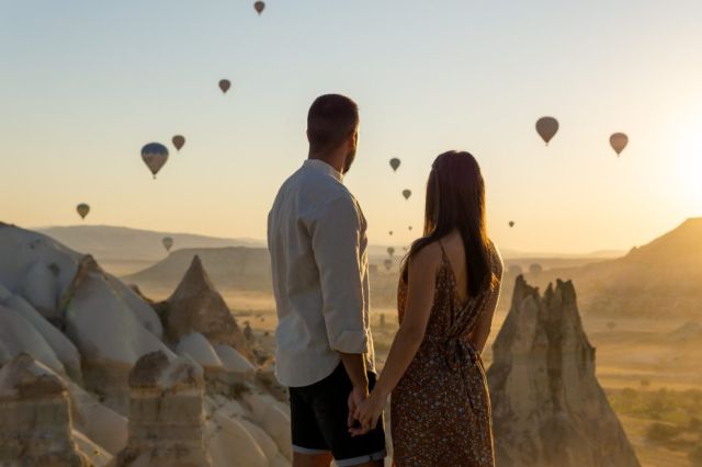 Jeune couple se tenant la main et regardant le soleil se coucher sur les montagnes